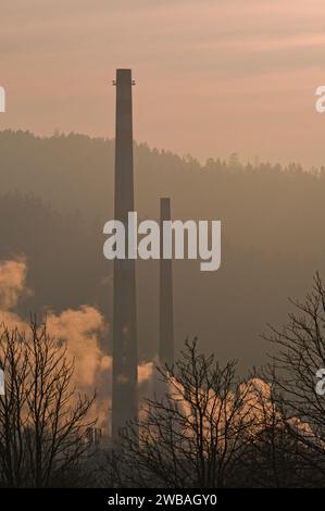 Hoher alter Schornstein im Industriegebiet und nebeliger Sonnenuntergang im Hintergrund. Roznov Pod Radhostem, Tschechische republik. Stockfoto