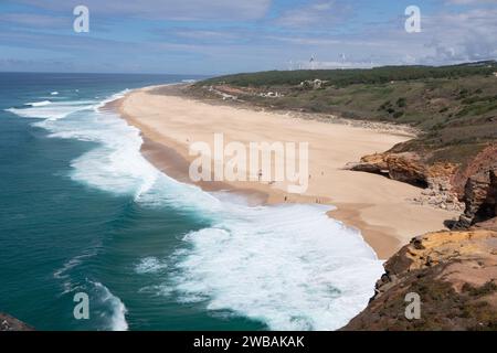 Rollende Wellen am Nordstrand Nazare Portugal mit Windturbinen in der Ferne Stockfoto