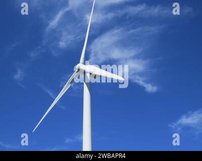 Eine Nahaufnahme einer Windkraftanlage, die hoch steht vor einem Hintergrund aus weißen Wolken in einem hellblauen Himmel Stockfoto