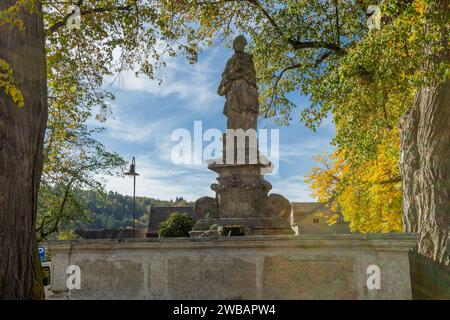 Svojsin, Tschechische Republik - 13. Oktober 2023: Blick auf den Steinbrunnen mit Johannes Nepomuk-Statue, umgeben von gelben und grünen Blättern. Sonnig Stockfoto