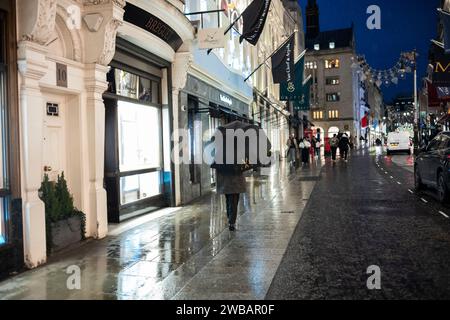 Käufer trotzen dem kalten Winter bei eisigen Schneeregen und Regenschauern auf der Old Bond Street, Londons luxuriöses Designerlabel Street, England, Großbritannien Stockfoto