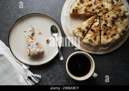 Draufsicht auf gebissenes Stück Kuchen auf dem Teller, ganzen Kuchen und eine Tasse schwarzen Kaffee Stockfoto