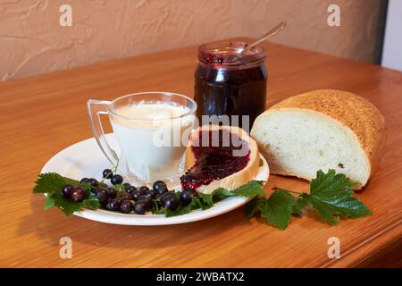 Milch mit Brot und Marmelade mit Johannisbeere auf dem Tisch Stockfoto