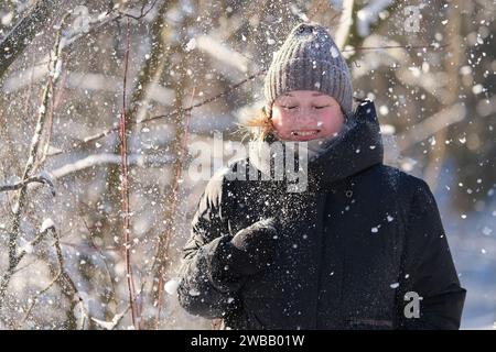 Porträt einer glücklichen jungen Frau, die an einem sonnigen Wintertag durch den Wald geht. Schneefall im Winterwald. Konzept von Spaß, Entspannung. Stockfoto