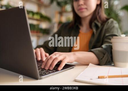 Frau, die an ihrem Laptop arbeitet, am Arbeitsplatz sitzt und sich auf die Hände konzentriert Stockfoto