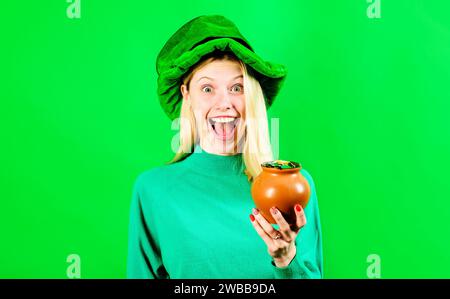 Patrick's Day-Feier. Pot mit Geld für Patricks Party. Glückliches blondes Mädchen im Leprechaun-Kostüm mit einem Topf Gold. Lächelnde Frau rein Stockfoto