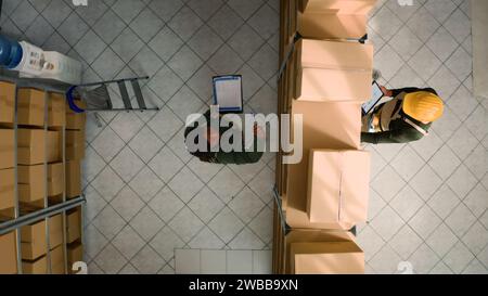 Top-Down-Ansicht der Logistikkoordinatoren, die Kartonpakete auf Mängel im Lager untersuchen. Mitarbeiter im Lagerraum sorgen dafür, dass Lagerbestände und Lagerbestände gut organisiert sind Stockfoto