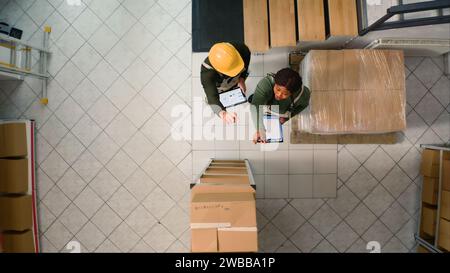 Top-Down-Ansicht der Lagermitarbeiter, die die Ergebnisse nach der Inspektion von Papppaketen vergleichen. Mitarbeiter des Versandzentrums sorgen dafür, dass Lagerbestände und Lagerbestände gut organisiert sind Stockfoto