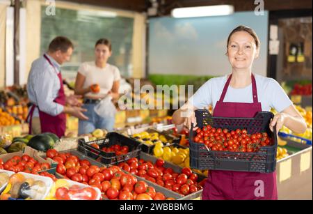 Erfolgreiche weibliche Besitzerin eines Gemüsegeschäfts, der Kiste mit Kirschtomaten hält Stockfoto