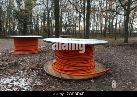 Zwei hölzerne Rollen mit einem orangefarbenen Kabel, die auf dem Boden liegen und mit Herbstblättern übersät sind. Stockfoto