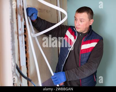 Klempner installiert neue Kunststoffrohre in speziellen Kästen in der Wand des im Bau befindlichen Hauses Stockfoto