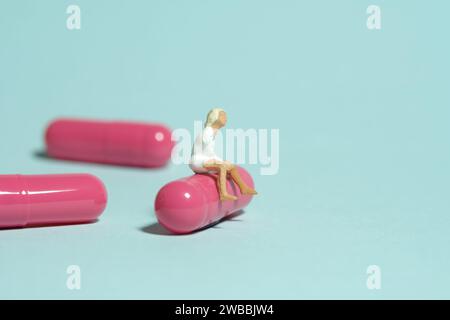 Miniatur-Kleinkinder-Spielfiguren-Fotografie. Ein Teenager, der über einer rosa Medikamententablette sitzt. Isoliert auf blauem Hintergrund. Bild Foto Stockfoto