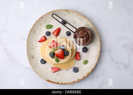 Köstliche Pfannkuchen serviert mit Beeren und Schokoladenaufstrich auf weißem Marmortisch, Blick von oben Stockfoto