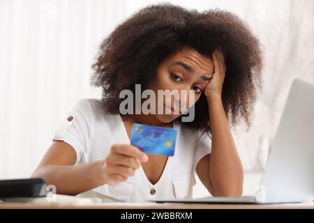 Verwirrte Frau mit Kreditkarte, die drinnen Budget plant. Schuldenproblem Stockfoto