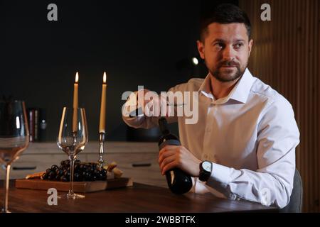 Romantisches Abendessen. Mann öffnet eine Weinflasche mit Korkenzieher am Tisch drinnen Stockfoto