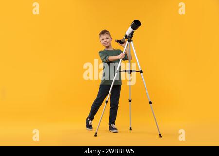 Glücklicher kleiner Junge mit Teleskop auf orangem Hintergrund Stockfoto