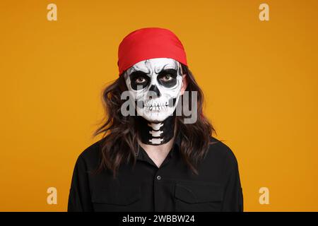 Mann im gruseligen Piratenkostüm mit Schädel-Make-up auf orangem Hintergrund. Halloween-Feier Stockfoto