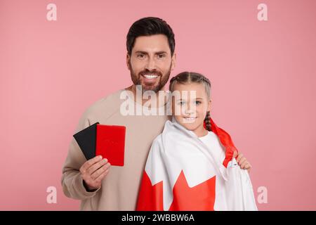 Einwanderung. Glücklicher Mann mit Pässen und seine Tochter mit kanadischer Flagge auf rosa Hintergrund Stockfoto