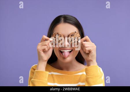 Junge Frau mit Schokoladenchips-Keksen auf lila Hintergrund Stockfoto