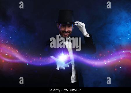 Ein lächelnder Zauberer zeigt einen Trick auf dunklem Hintergrund Stockfoto