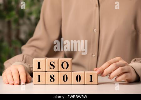 Frau, die die Abkürzung ISO und Nummer 18001 von Holzwürfeln auf weißem Tisch macht, Großaufnahme Stockfoto