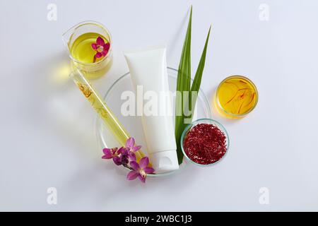 Draufsicht eines weißen Kunststoffröhrenmodells für Kosmetik auf einer Petrischale mit Stigmas Safran, frischem Crocus Sativus, grünen Blättern dekoriert mit Stockfoto