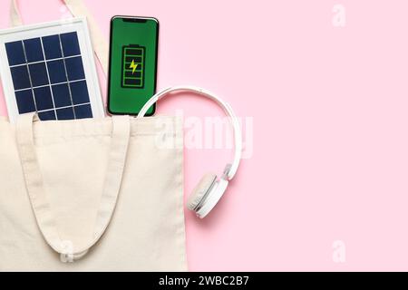 Tasche mit tragbarem Solarmodul, Mobiltelefon und Kopfhörern auf pinkfarbenem Hintergrund Stockfoto