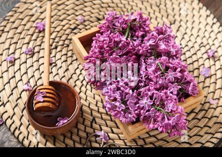 Korbmatte und Schachtel mit wunderschönen Fliederblumen mit Honig auf braunem Holzhintergrund Stockfoto