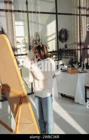 In der Wohnung strahlt eine lebhafte junge Frau mit weihnachtlicher Rentiermaske vor Freude. Stockfoto