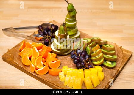 Eine lebhafte Auswahl an frischen Früchten mit einem Herzstück einer spiralgeschnittenen Birne, umgeben von Orangen, Kiwis, Trauben und Ananas auf einem Holz Stockfoto