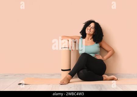 Sportliche junge Frau mit Yogamatte auf dem Boden vor beigefarbenem Hintergrund Stockfoto