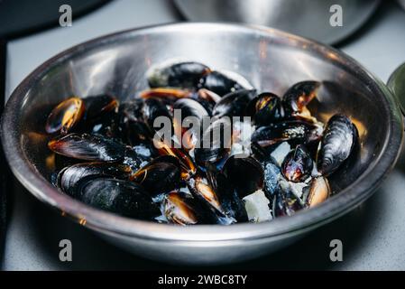 Eine Metallschale mit Muscheln, die sich mit offenen Muscheln auftauen lassen, unterstreicht den Zubereitungsprozess in der Küche. Stockfoto