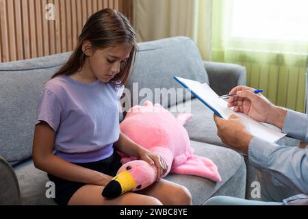 Nahaufnahme eines Arztpsychologen, der ein Notizbuch hält und Notizen macht, während er mit einem kleinen Mädchen über die psychologische Therapiesitzung sprach. Stockfoto