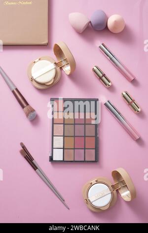 Auf pastellrosa Hintergrund, Make-up Set: Lidschatten, Lippenstift, Kissen, Schwamm und Make-up Pinsel kreativ dekoriert. Konzept für Werbekosmetik Stockfoto