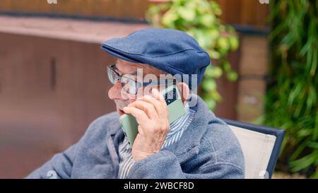 Senior-Mann, der mit dem Handy spricht, sitzt draußen und ist geriatrisch Stockfoto