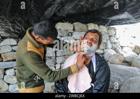 Rudarprayag, Uttarakhand, Indien, 18. Juni 2014, Indian Barber rasiert den Bart des Mannes im traditionellen Stil. In Indien ist der traditionelle Rasierstil sehr beliebt, bei dem Barber sich in einem offenen Geschäft oder unter einem Baum rasiert. Stockfoto