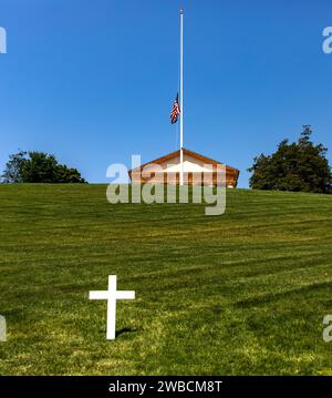 Ein weißes Marmorkreuzgrab vor dem pantheon und Haus auf dem Arlington National Cemetery, einem Militärfriedhof in Washington DC (USA). Stockfoto