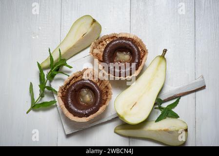 Schokoladen-Mini-Kuchen mit Birnengelee in der Mitte. In Papierkörben, auf einem hellen Holztisch, mit frischen Birnenhälften Stockfoto