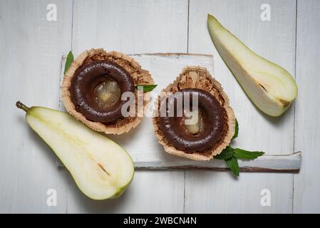 Schokoladen-Mini-Kuchen mit Birnengelee in der Mitte. In Papierkörben, auf einem hellen Holztisch, mit frischen Birnenhälften Stockfoto