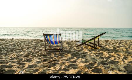 Zwei leere Liegen am Strand bei Sonnenuntergang. Liegestühle oder Liegestühle auf Sand am Strand. Sommerurlaub Reiseberufe Konzept. Minimalistisch Stockfoto