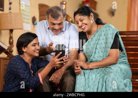 Indische Teenager-Tochter zeigt Handy-App für Eltern mittleren Alters zu Hause - Konzept des Social Media Sharing, Internet oder Technologie und Familie Stockfoto