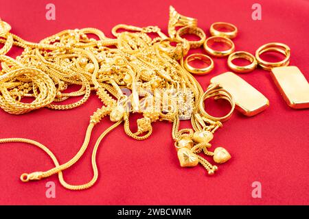 Viele goldene Ketten und Goldbarren auf rotem Samthintergrund. Stockfoto