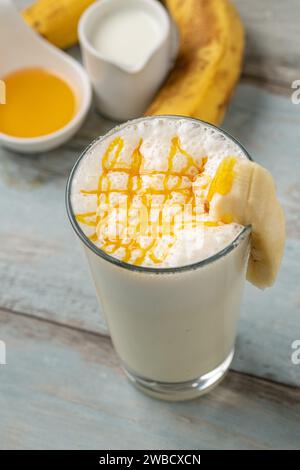 Milch mit Honig und Banane im Glas auf Holztisch Stockfoto