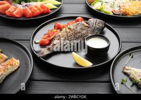 Gegrillter dorado-Fisch, serviert auf einem schwarzen Teller in einem Restaurant. Grillmenü in einem Restaurant. Verschiedene Gerichte auf dem Tisch Stockfoto