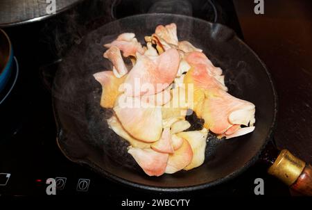 Rosafarbene Austernpilze werden in Butter in einer schwarzen, gusseisernen Pfanne serviert - lecker zum Frühstück Stockfoto