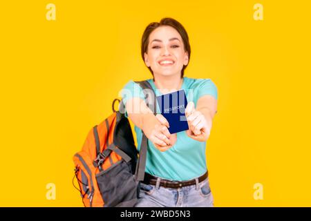Happy Enjoy Woman in grünem T-Shirt mit orangem Rucksack und Pass auf gelbem Hintergrund. Reisekonzept Stockfoto
