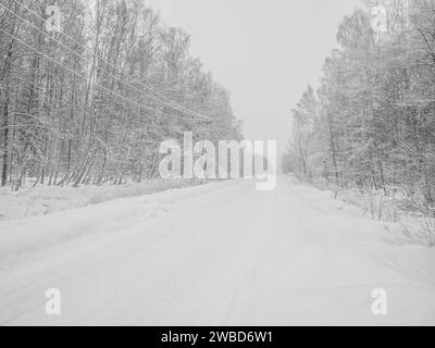 Winterstraße durch einen verschneiten Wald bei Schneefall. Eine schneebedeckte Straße, die sich an einem Wintertag in die Ferne zieht. Stockfoto