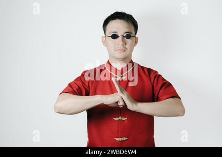 Asiatischer Mann in traditioneller Tracht mit Geste der Glückwünsche auf weißem Hintergrund. Chinesisches Neujahrskonzept. Gong Xi Fa Cai. Stockfoto