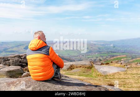 Bärtiger Mann in orangefarbener Jacke, der sich allein auf dem Gipfel des Berges entspannt und bei Sonnenaufgang heißen Kaffee trinkt. Travel Lifestyle Konzept der Nationalpark Stockfoto