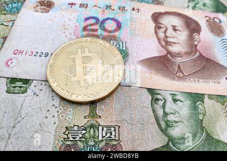 Nahaufnahme einer goldenen Bitcoin-Münze auf einem Stapel chinesischer Renminbi-Banknoten. Stockfoto